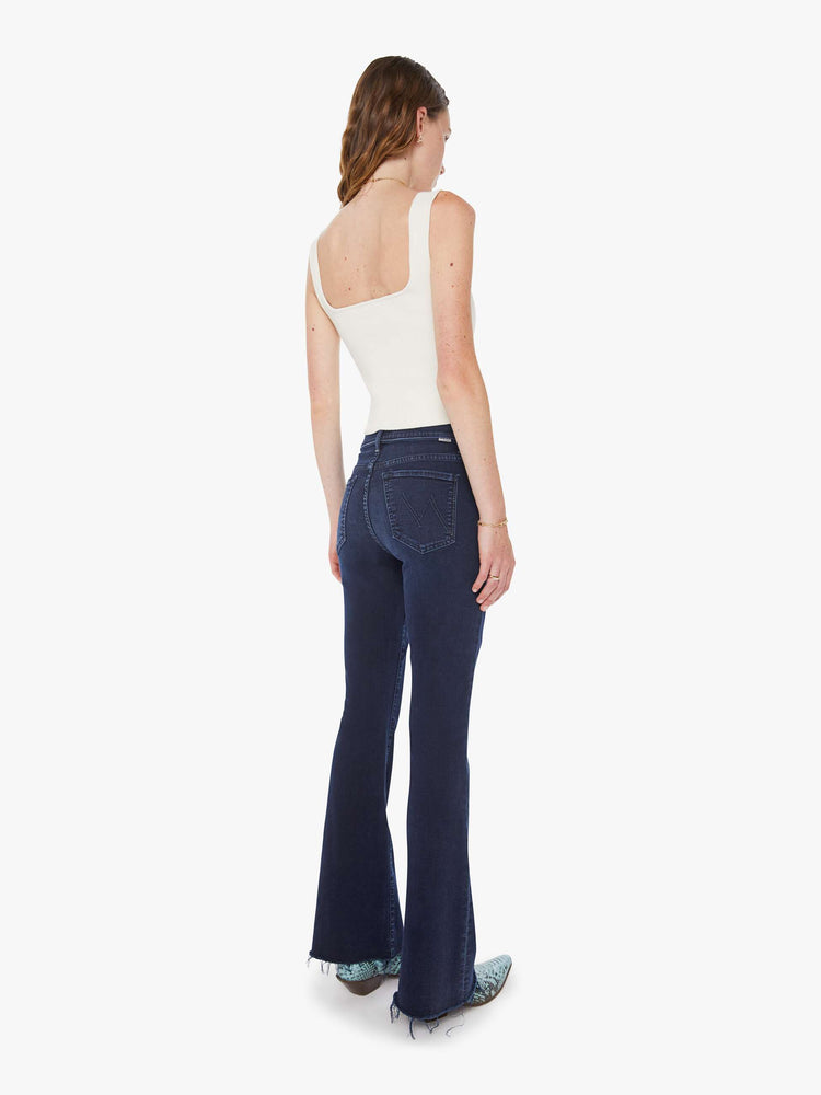 Back view of a woman in a dark blue wash mid-rise flare with a 31-inch inseam and frayed hem.