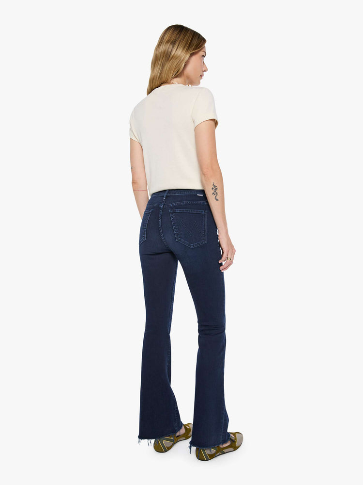 Back view of a woman in a dark blue wash mid-rise flare with a 31-inch inseam and frayed hem.