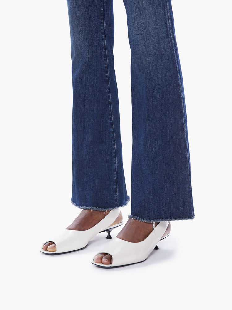 Side close up view of a woman mid-rise flare has a 31-inch inseam with a frayed hem in dark blue.