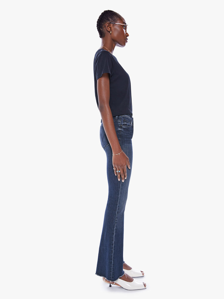 Side view of a woman mid-rise flare has a 31-inch inseam with a frayed hem in dark blue.