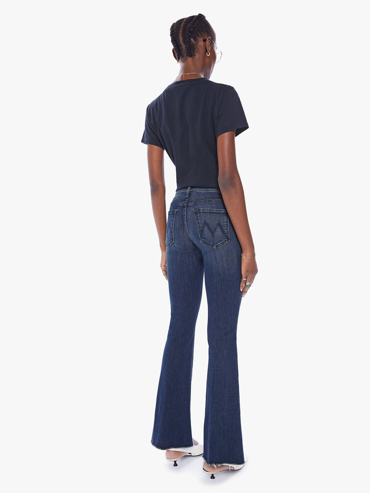Back view of a woman mid-rise flare has a 31-inch inseam with a frayed hem in dark blue.
