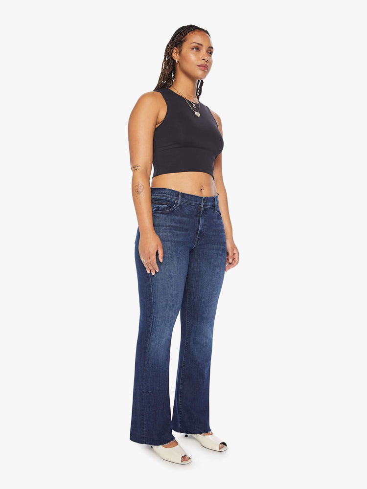 Side angle view of a woman mid-rise flare has a 31-inch inseam with a frayed hem in dark blue.