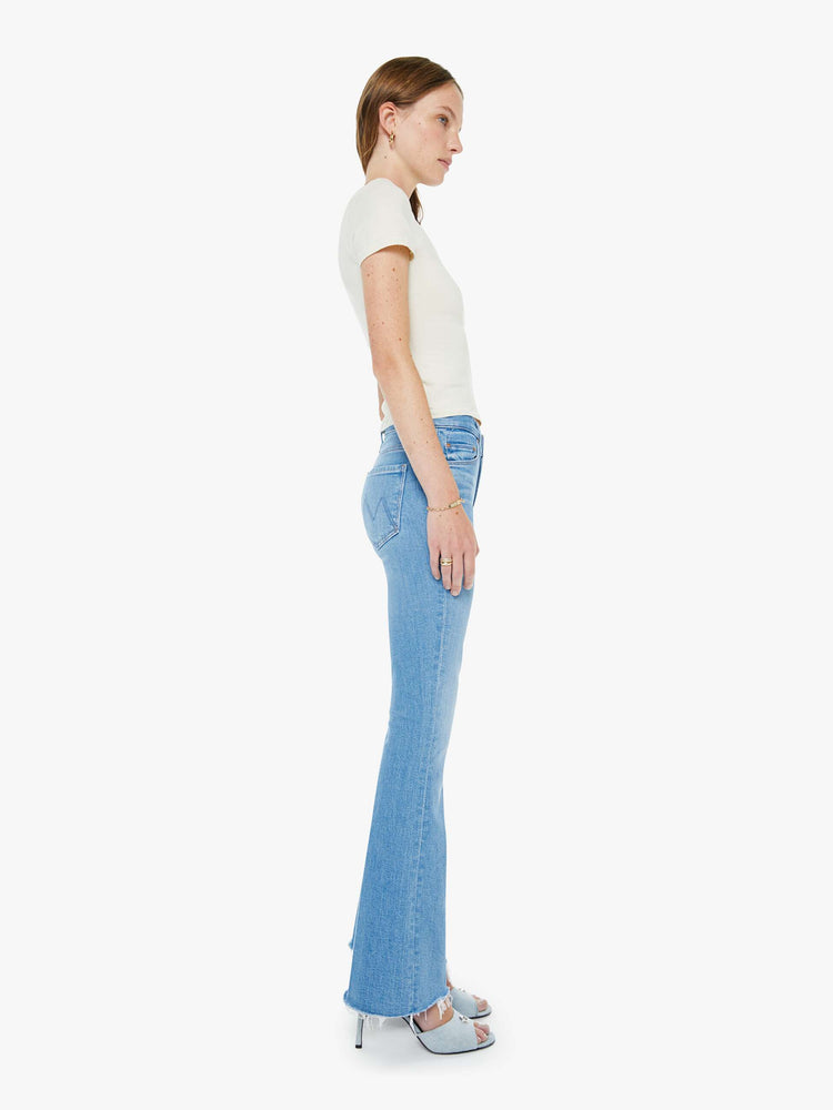 Side view of a woman in a light blue mid-rise flare has a zip fly, 31-inch inseam and a frayed hem.