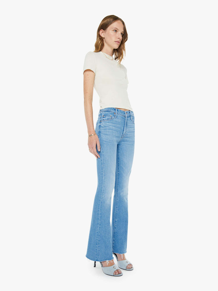 Front view of a woman in a light blue mid-rise flare has a zip fly, 31-inch inseam and a frayed hem.