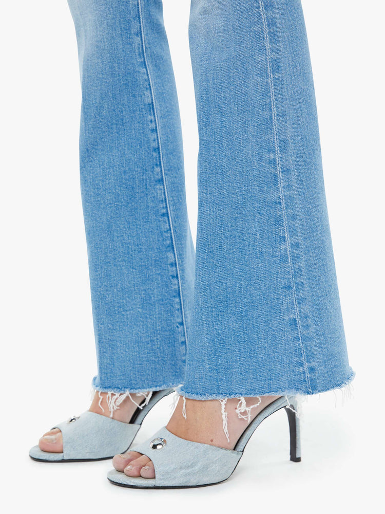 Hem close up view of a woman in a light blue mid-rise flare has a zip fly, 31-inch inseam and a frayed hem.