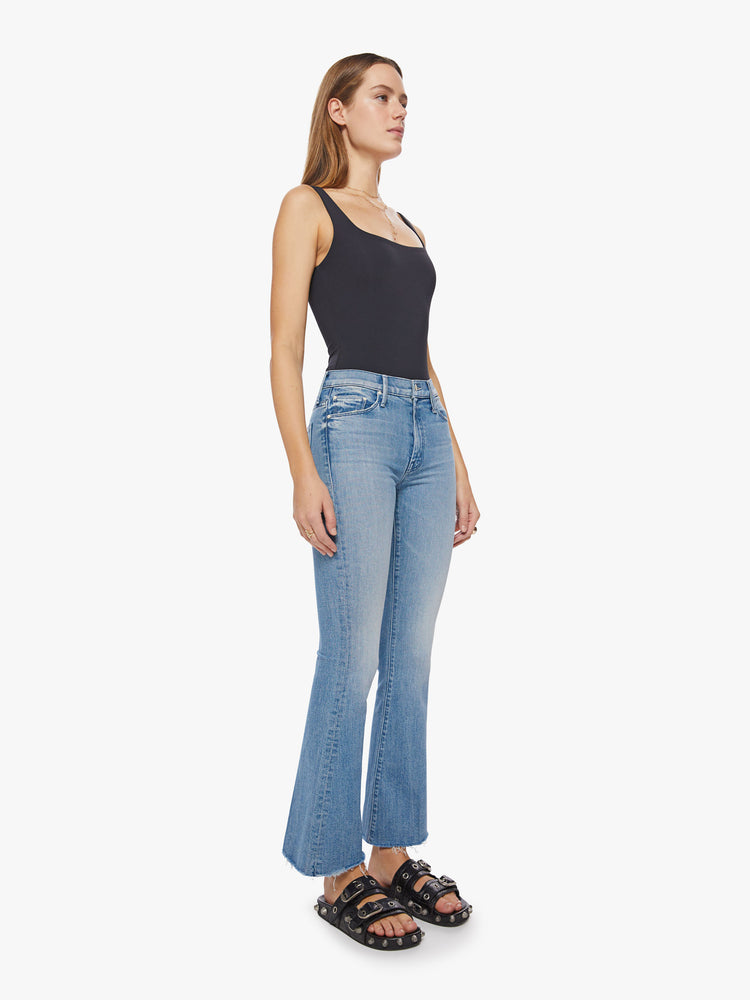 Side angle view of a woman flare jean has a mid rise with a 31-inch length inseam and a frayed hem in a light blue wash.