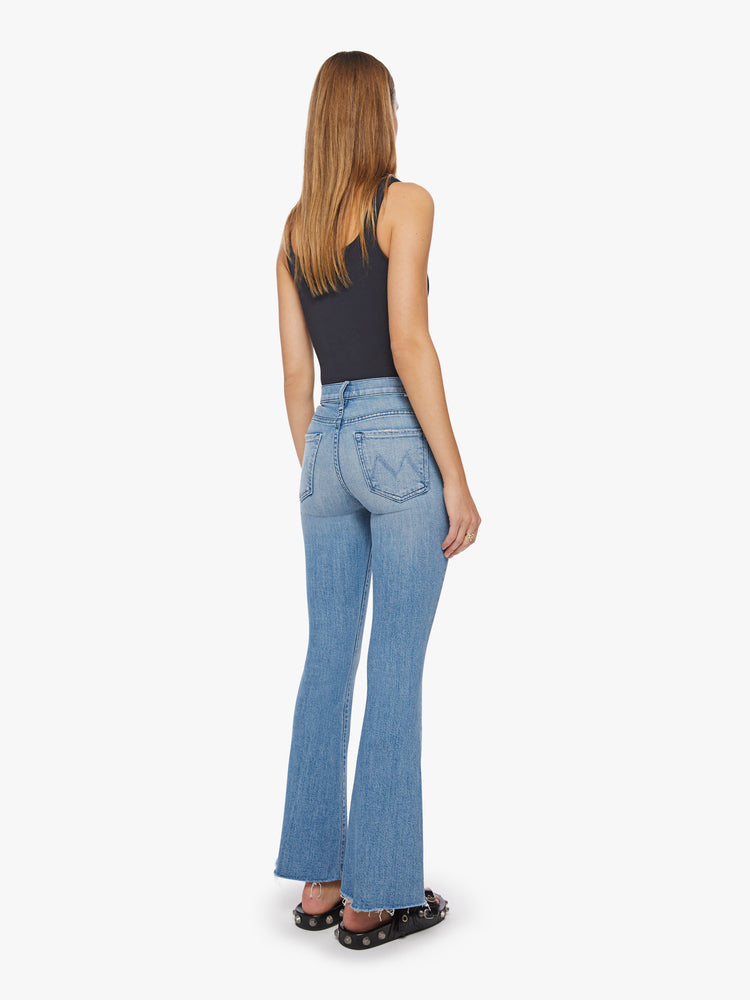 Back view of a woman flare jean has a mid rise with a 31-inch length inseam and a frayed hem in a light blue wash.