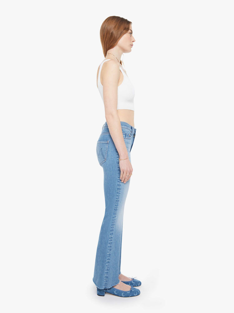 Side view of a woman in a light blue  mid-rise flare has a zip fly, 32.25-inch inseam and a frayed hem. 