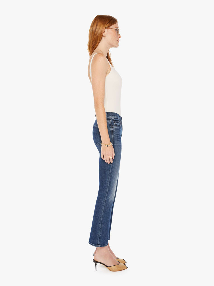 Side view of a womens dark denim wash jean featuring a mid rise and a ankle length flare.