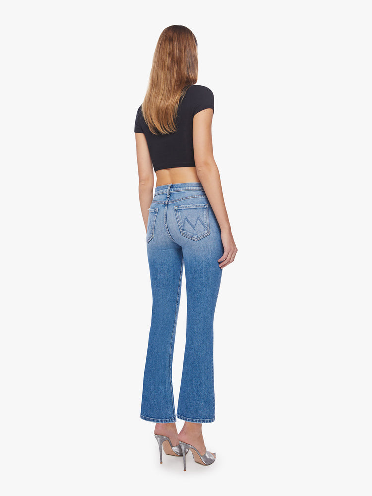 Back view of a woman light blue wash, narrow flare jeans with a high rise and an ankle-length inseam with a clean hem.