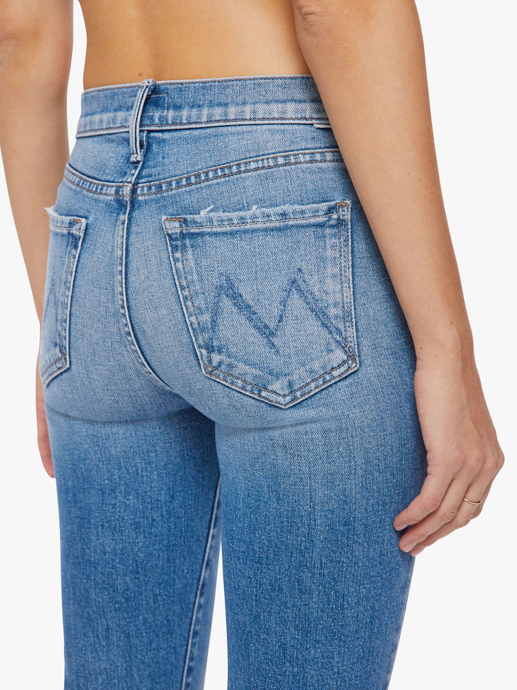 Waist back close up view of a woman light blue wash, narrow flare jeans with a high rise and an ankle-length inseam with a clean hem.