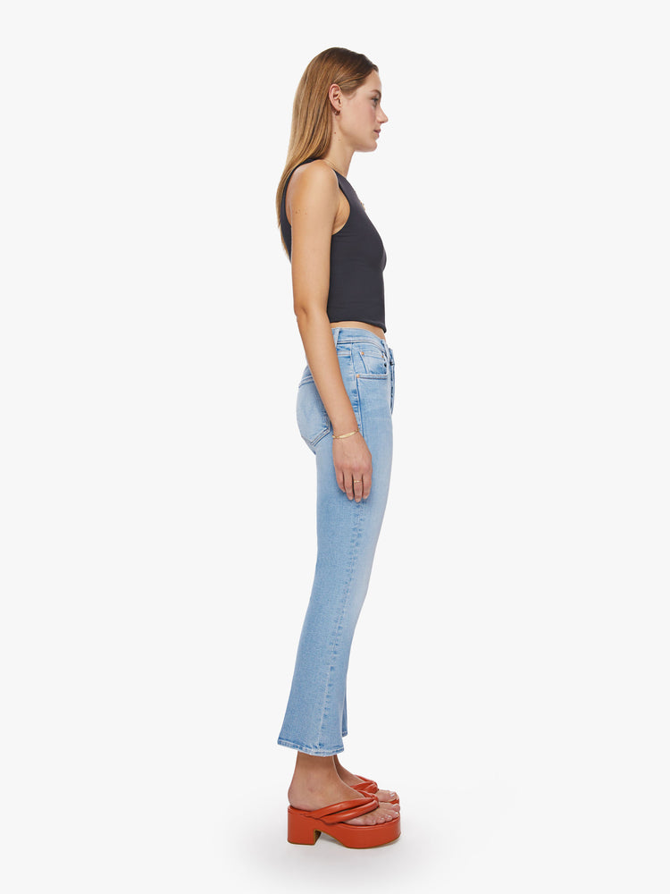 Side view of a woman high-rise flare with a button fly and a clean ankle-length hem in a light blue wash.