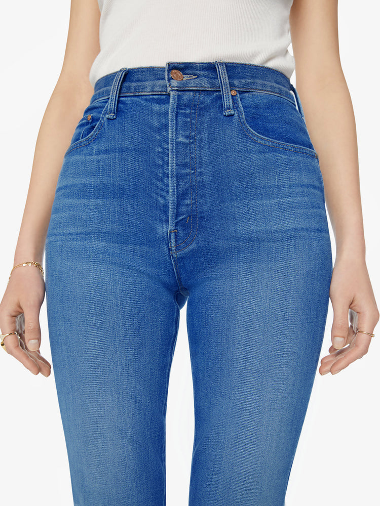 Waist view of a woman high-rise flare with a button fly and a clean ankle-length hem in a mid-blue wash.