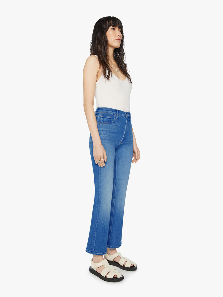 Side angle view of a woman  high-rise flare with a button fly and a clean ankle-length hem in a mid-blue wash.