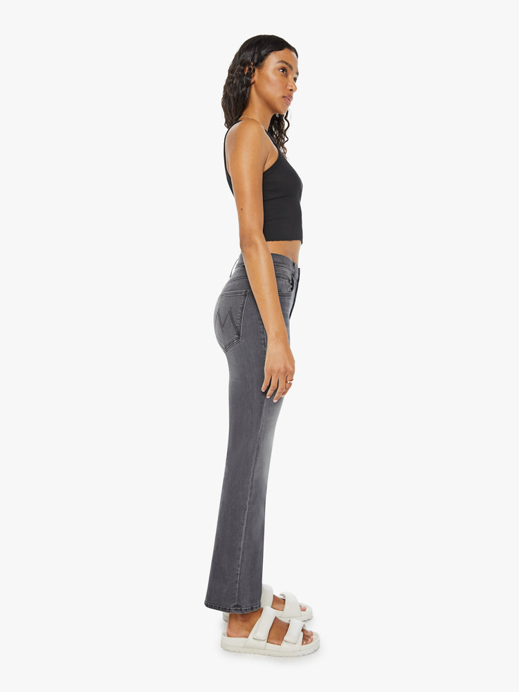 Side angle view of a woman in high-rise flare with a button fly and a clean ankle-length hem dark grey wash.