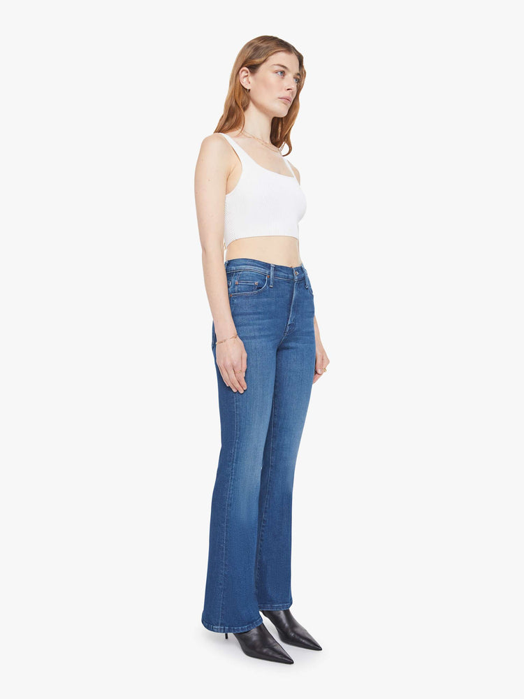 Side angle view of a woman in a med blue flare jean with a mid rise, zip fly, 31-inch inseam and a clean hem.