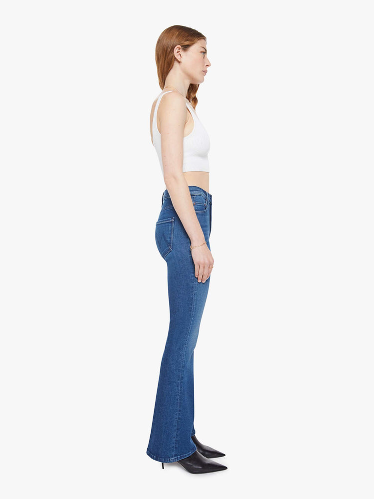 Side angle view of a woman in a med blue flare jean with a mid rise, zip fly, 31-inch inseam and a clean hem.