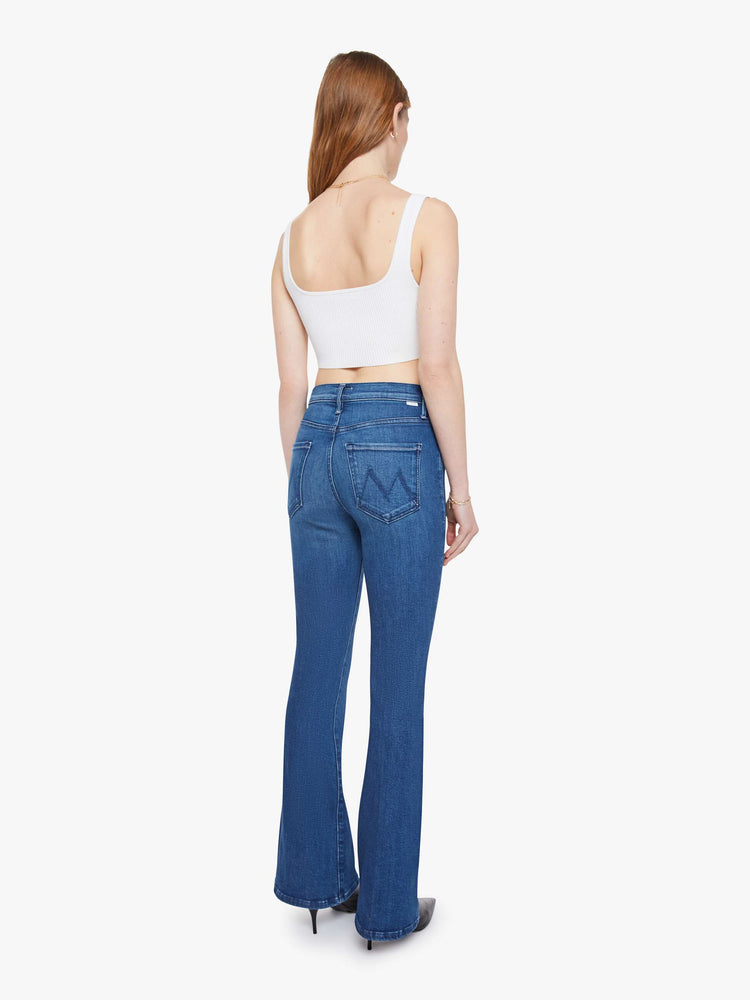Back view of a woman in a med blue flare jean with a mid rise, zip fly, 31-inch inseam and a clean hem.