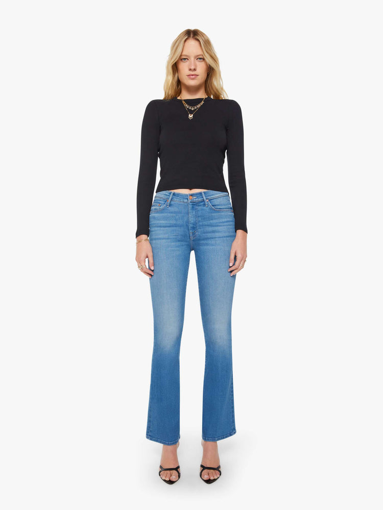 Front view of a woman in a med blue flare jean has a mid rise with a 31-inch inseam and a clean hem.