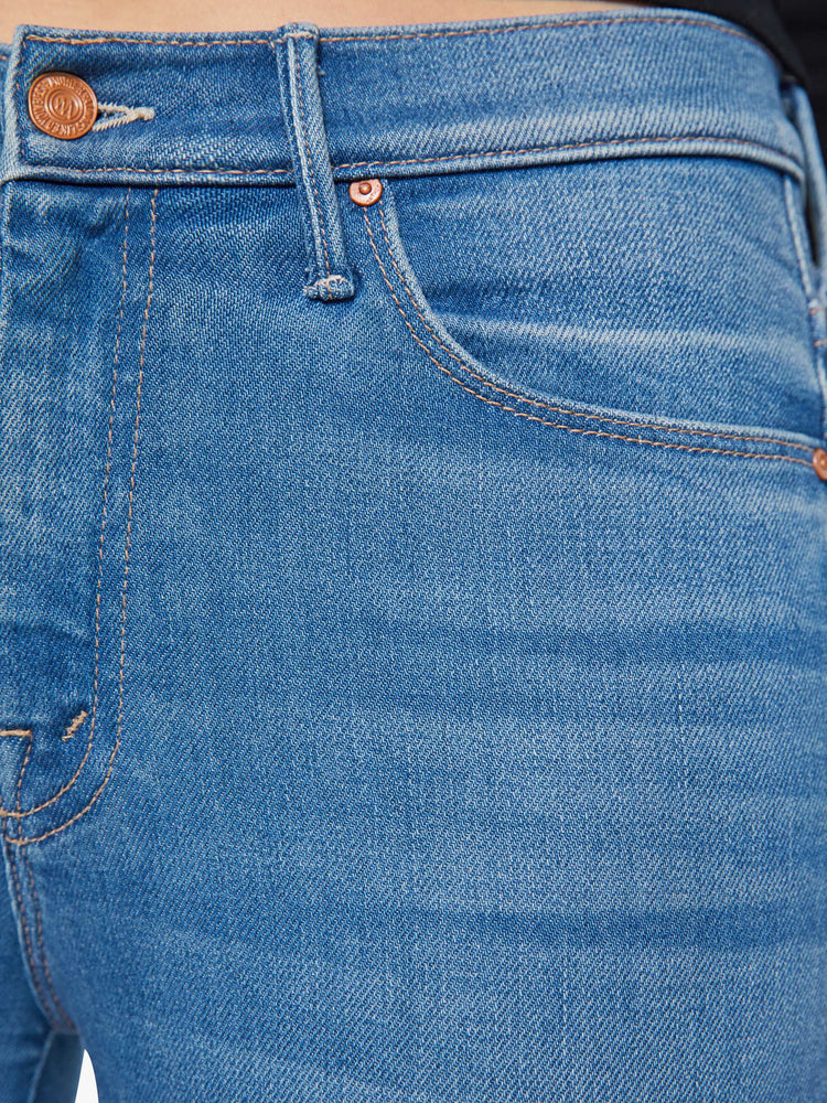 Clos up view of a woman in a med blue flare jean has a mid rise with a 31-inch inseam and a clean hem.