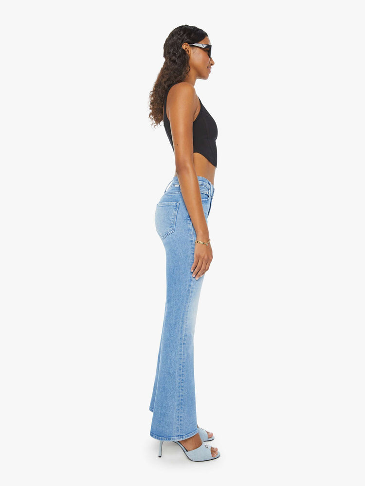 Side view of a woman in a mid rise light blue flare jean with a clean hem.