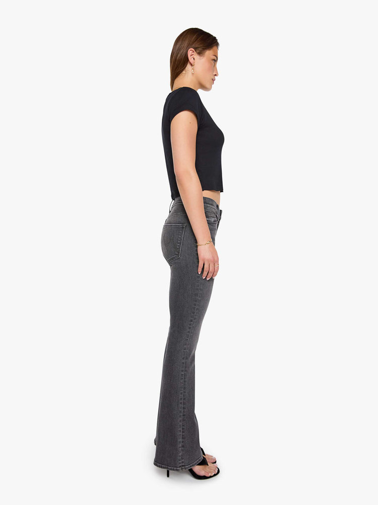 Side view of a woman in a faded black flare jean with a mid rise and 31-inch inseam and a clean hem. 