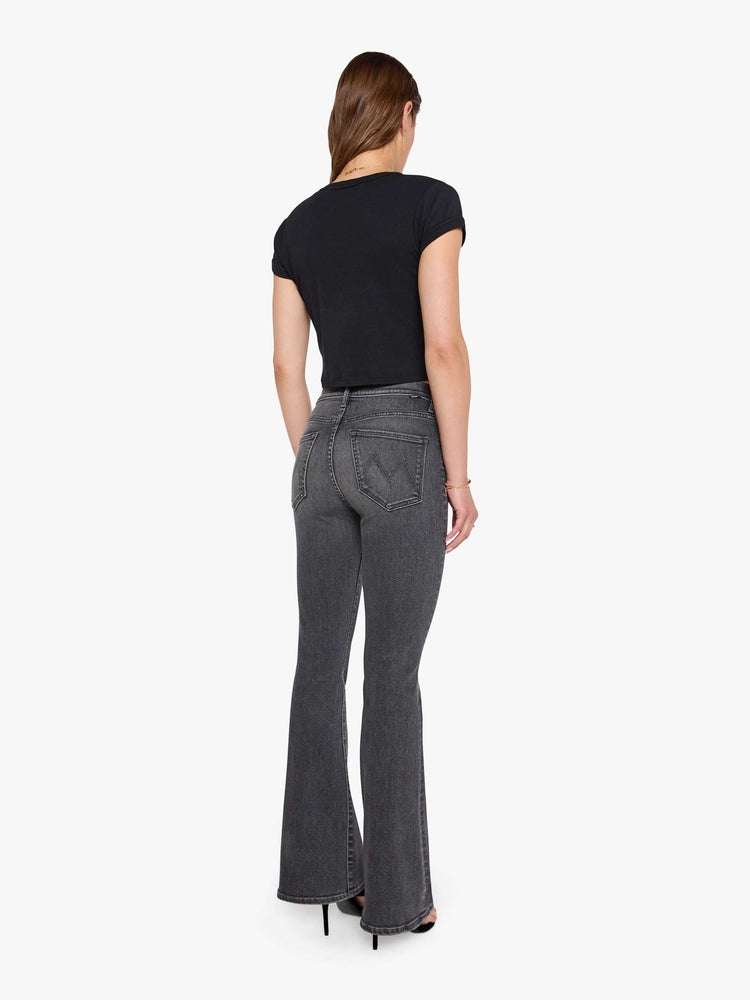 Back view of a woman in a faded black flare jean with a mid rise and 31-inch inseam and a clean hem. 