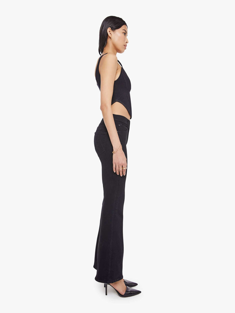 Side view of a woman in a dark black flare jean with a mid rise and 31-inch inseam and a clean hem. 