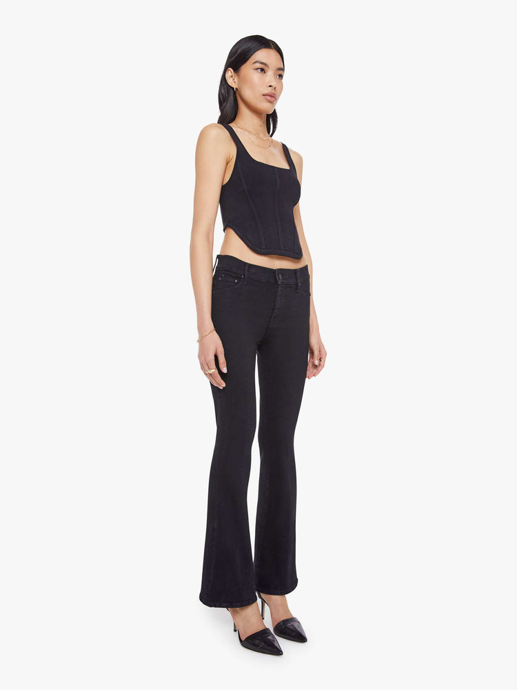 Side angle view of a woman in a dark black flare jean with a mid rise and 31-inch inseam and a clean hem. 