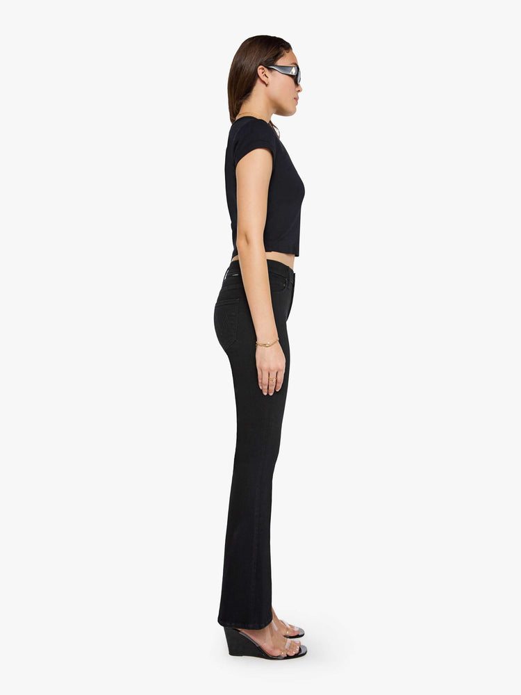 Side view of a woman in a dark black flare jean with a mid rise and 31-inch inseam and a clean hem. 