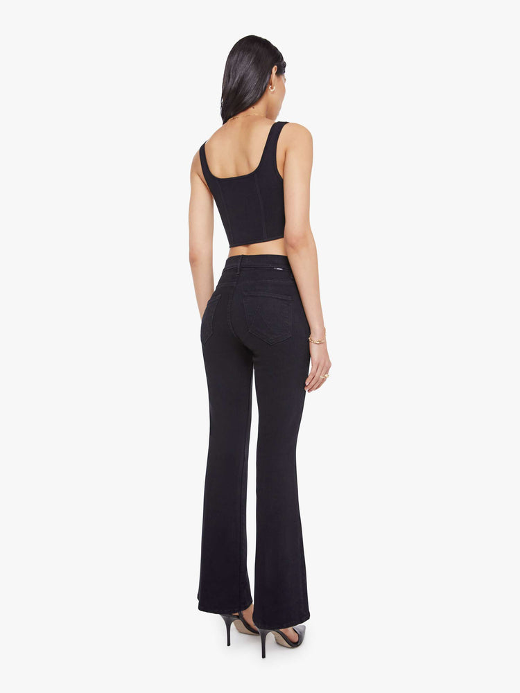 Back view of a woman in a dark black flare jean with a mid rise and 31-inch inseam and a clean hem. 