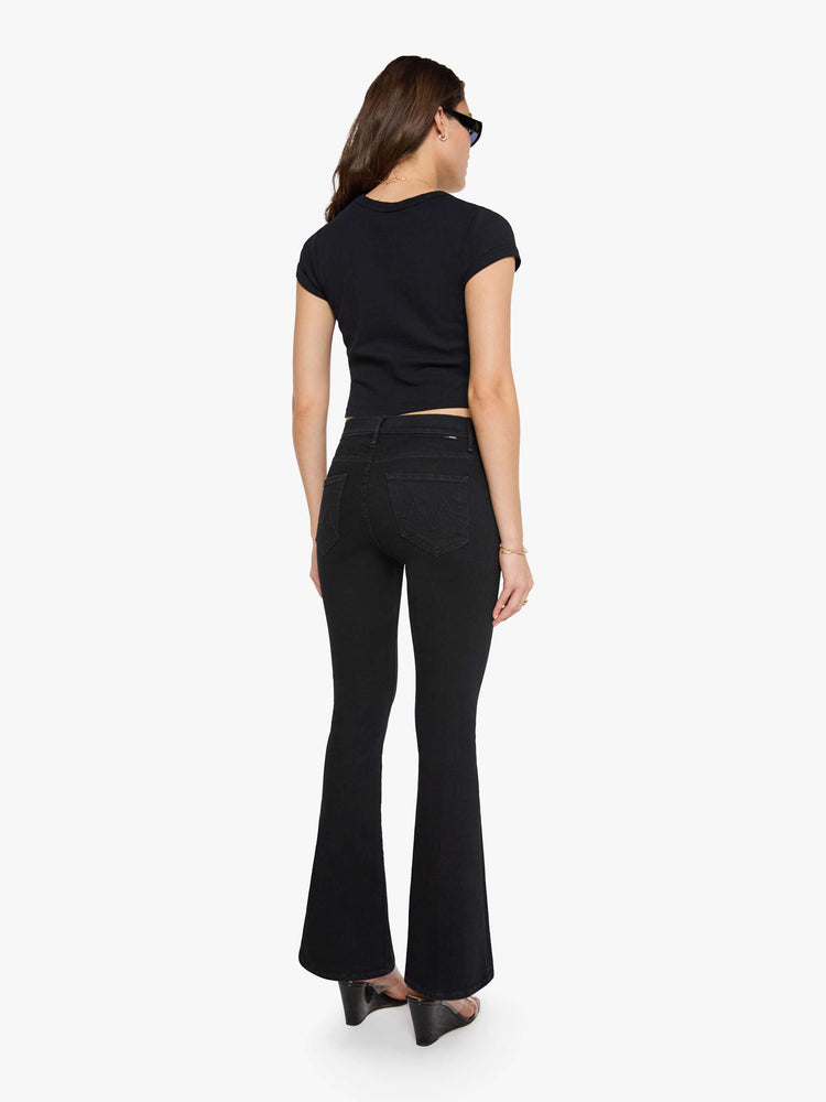 Back view of a woman in a dark black flare jean with a mid rise and 31-inch inseam and a clean hem. 