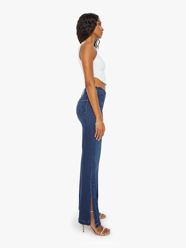 Side view of a woman high-waisted wide-leg jeans with a long inseam and a thick side-slit hem in a dark blue wash.