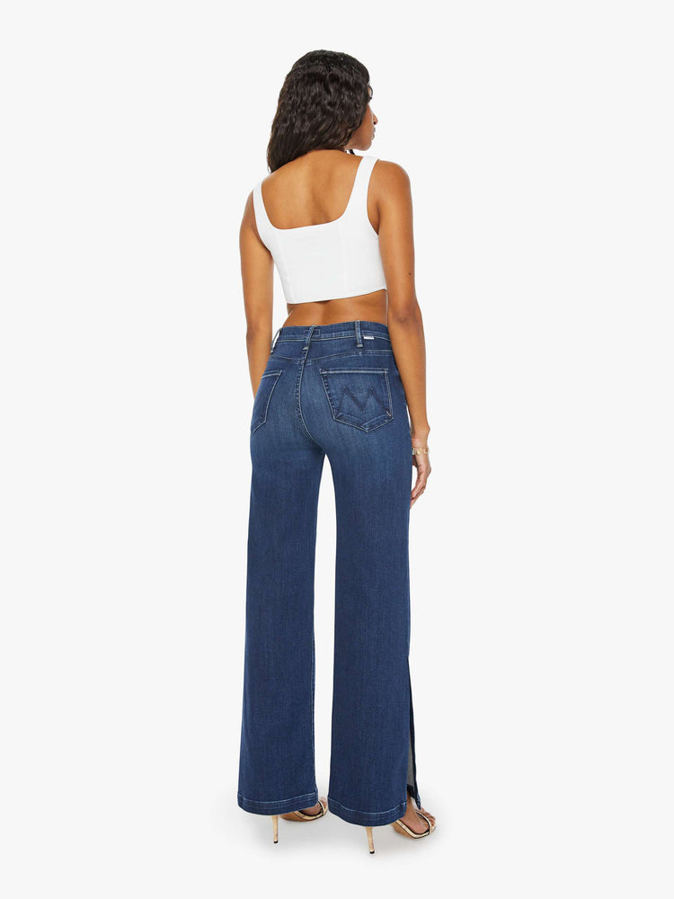 Back view of a woman high-waisted wide-leg jeans with a long inseam and a thick side-slit hem in a dark blue wash.
