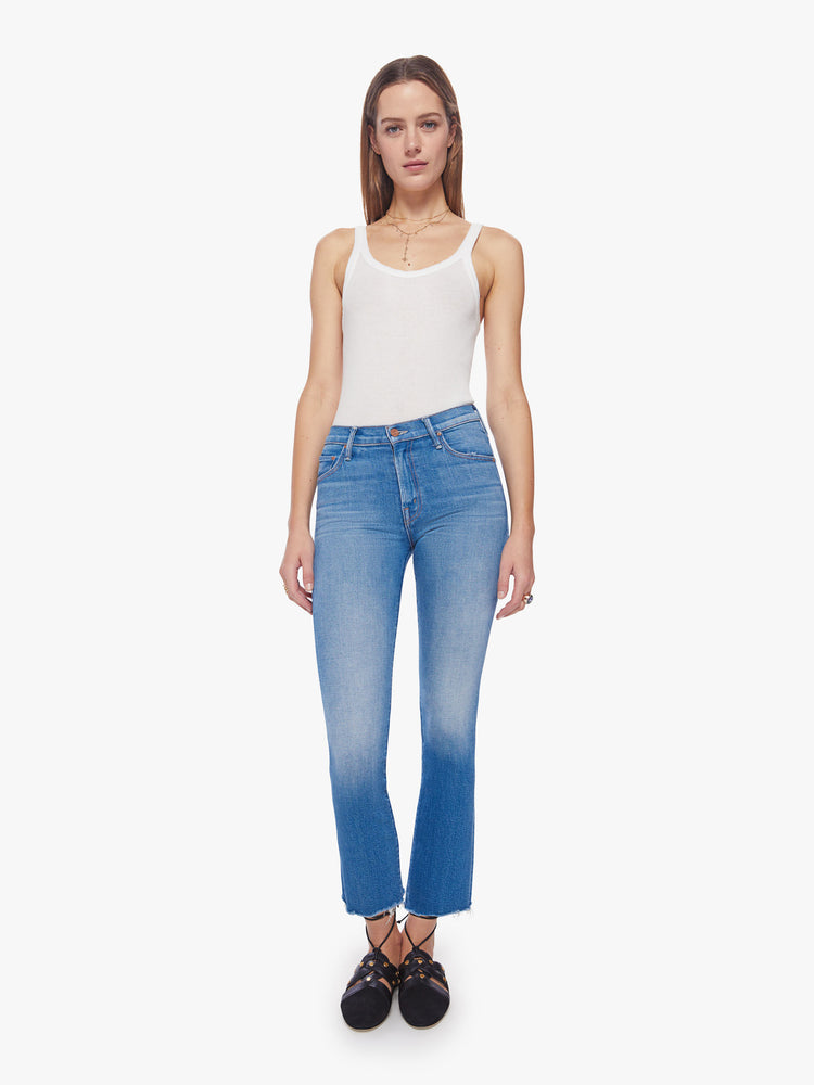 Front view of a woman mid blue wash mid-rise bootcut has an ankle-length inseam and raw hem.