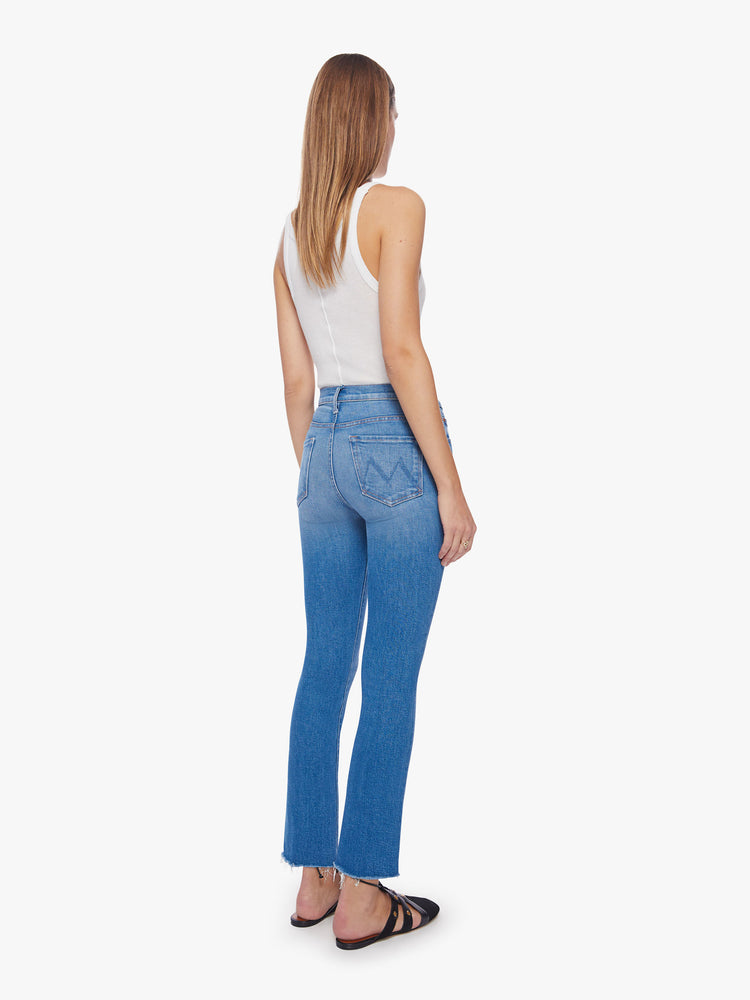Back view of a woman mid blue wash mid-rise bootcut has an ankle-length inseam and raw hem.