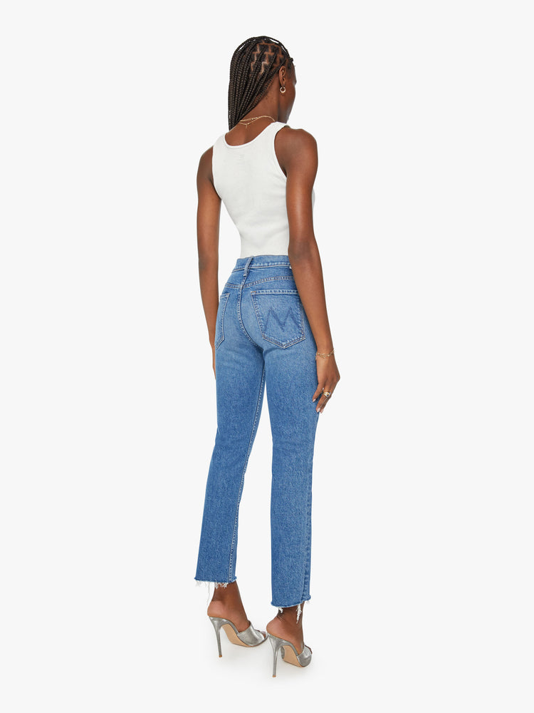 Back view of a woman high-rise jeans with a straight leg, button fly, ankle-length inseam and a frayed hem in a mid blue wash.