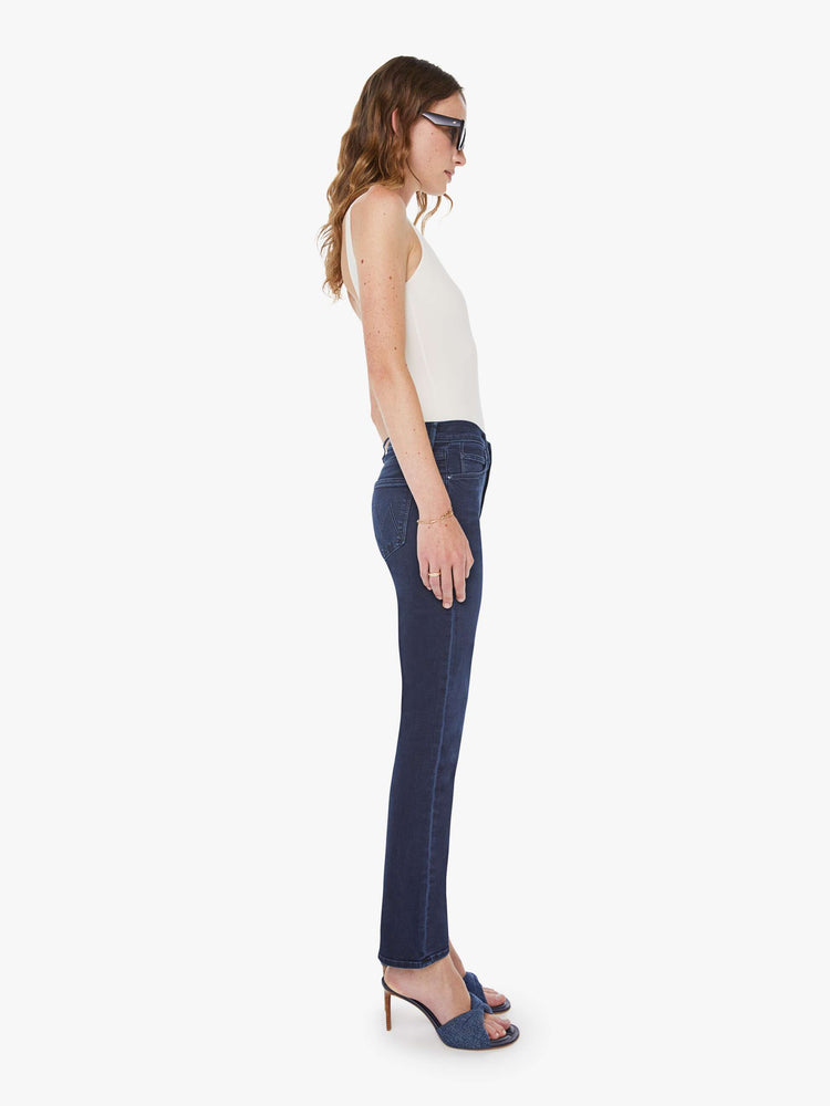 Side view of a woman in dark blue wash jeans with a mid-rise straight leg hits at the ankle with a clean hem.