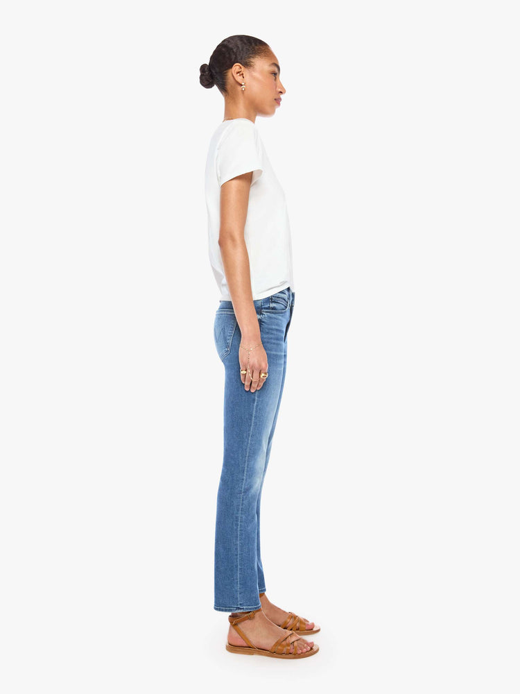 Side view of a womens classic medium blue wash denim jean featuring a mid rise, a slim straight leg, an ankle length clean hem, and subtle whiskering details.