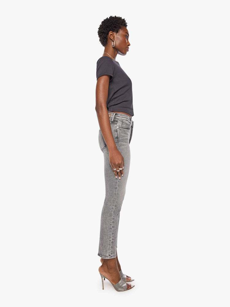 Side view of a woman in a mid-rise straight leg has a zip fly and hits at the ankle with a clean hem in a washed grey with whiskering and fading at the knees.