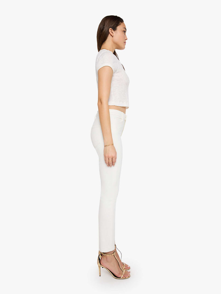 Side view of a model wearing white denim pants with a mid rise, slim straight leg, and a clean hem.