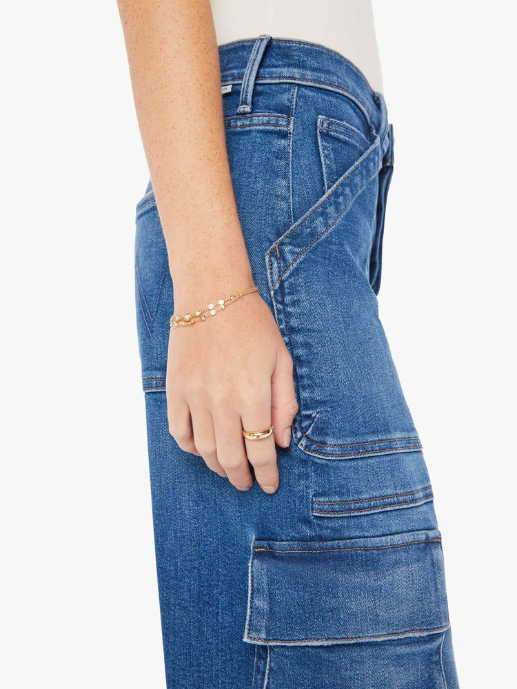 Side close up view of a womens medium blue wash cargo jean featuring a high rise.