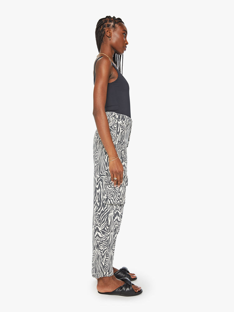 Side view of a woman high waisted cargo pant with a barrel leg, patch pockets and a long inseam with snaps at the hem with black and white zebra print.