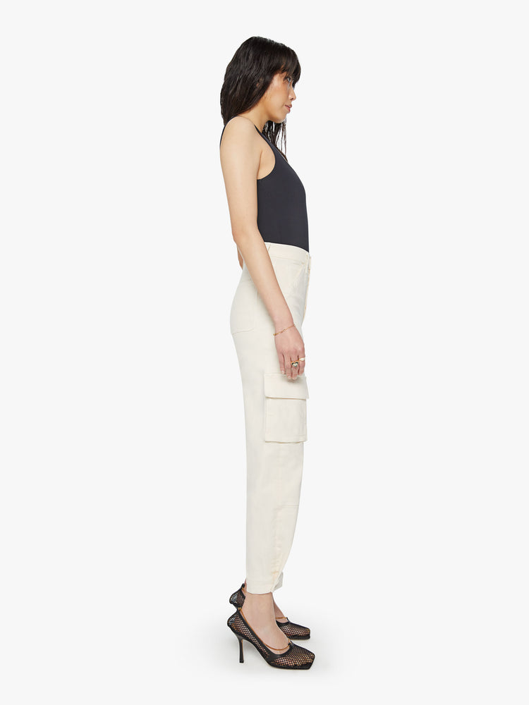 Side view of a woman super high waisted cargo pant with a barrel leg, patch pockets and a long inseam with snaps at the hem in an off-white color.