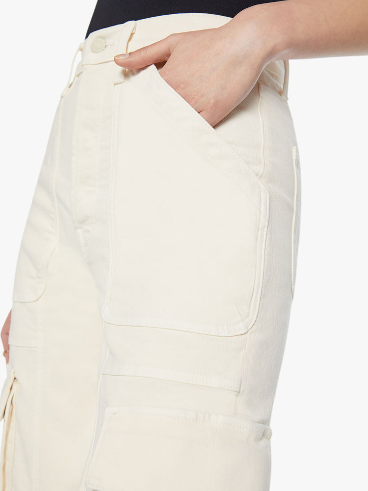 Close up view of a woman super high waisted cargo pant with a barrel leg, patch pockets and a long inseam with snaps at the hem in an off-white color.