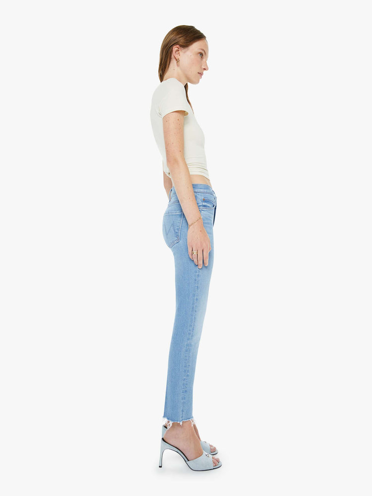 Side view of a woman in a light blue mid-rise jean has a straight leg, zip fly, cropped inseam and a frayed hem.