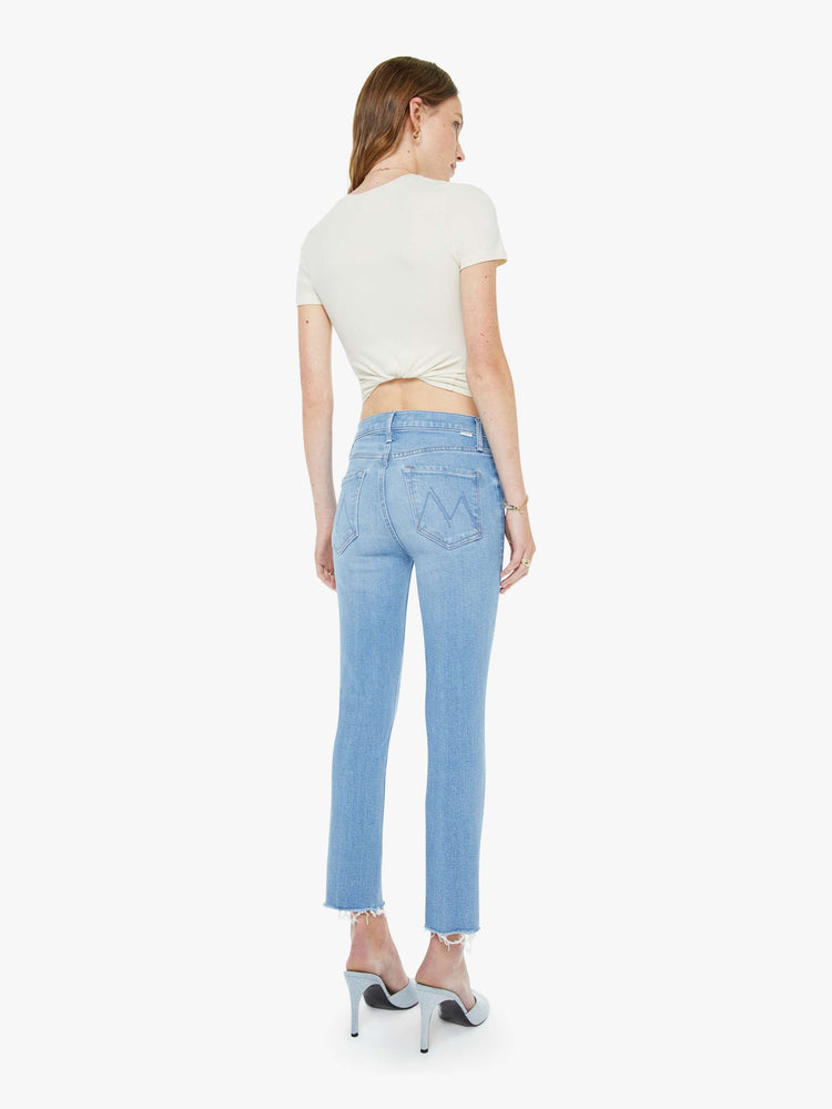 Back view of a woman in a light blue mid-rise jean has a straight leg, zip fly, cropped inseam and a frayed hem.