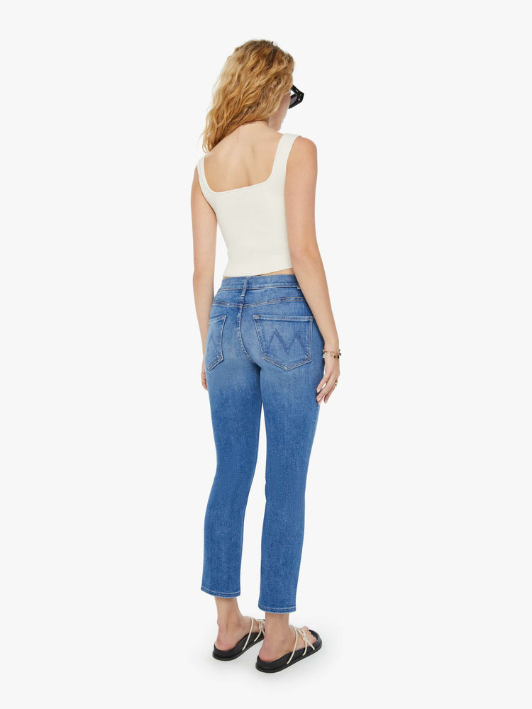 Back view of a woman in mid-blue straight leg jeans with a cropped hem and whiskering and fading at the knees. Styled with a white tank top. 