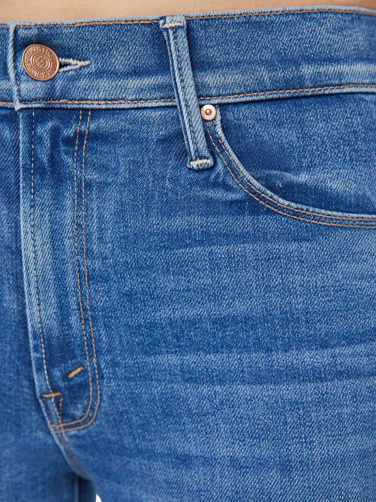 Detailed view of a woman in mid-blue straight leg jeans with a cropped hem and whiskering and fading at the knees. 