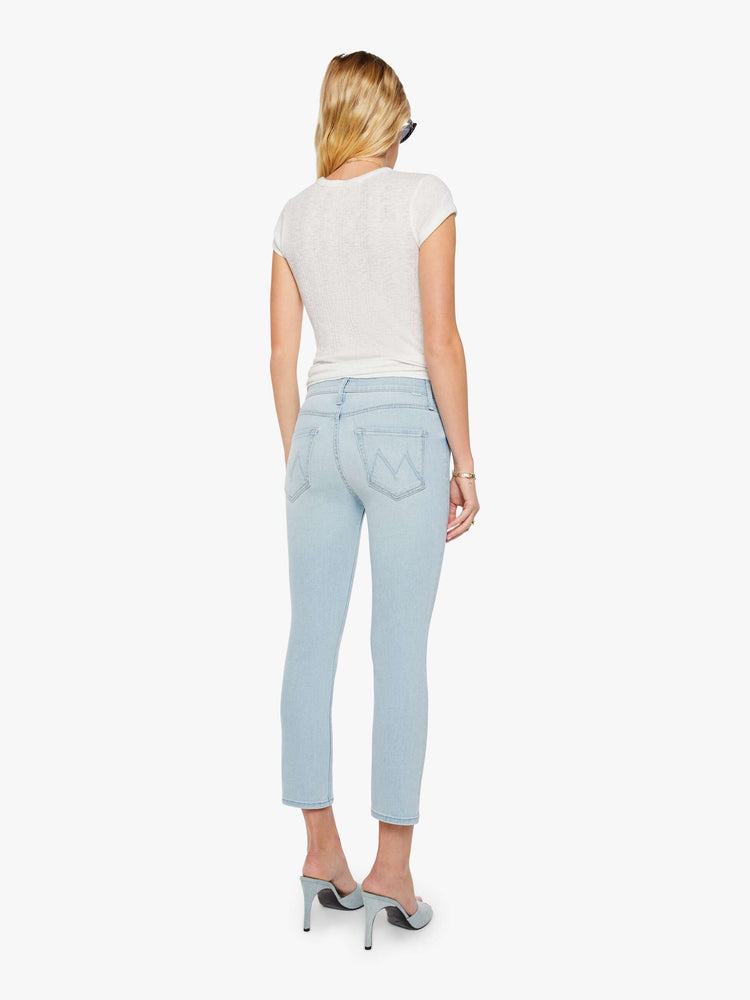 Back view of a woman in light blue mid-rise jean has a straight leg, zip fly, cropped inseam and a frayed hem.